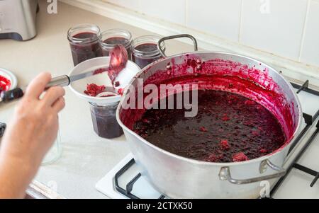 Preparazione della marmellata - versando la marmellata di more e mela da un recipiente per la conservazione caldo in un recipiente per marmellata pulito Foto Stock