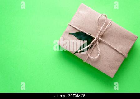 Confezione regalo avvolta in carta kraft legata con spago e decorata con due foglie verdi su sfondo verde chiaro. Idea presente fai da te. Concetto di zero sprechi Foto Stock