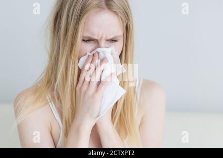 Giovane donna malata con un freddo che soffia il naso in una carta tissue a casa. Primo piano. Foto Stock