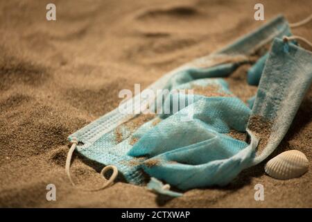 Rifiuti durante COVID-19. Scartato in maschere monouso per il viso del coronavirus. Inquinamento dell'ambiente, sulla spiaggia, impronta dell'uomo nella sabbia Foto Stock