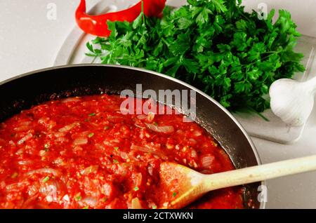 Salsa di Marinara. Salsa di pomodoro cotta in casa per pasta o spaghetti in padella con cucchiaio di legno. Prezzemolo verde fresco, peperoncino e aglio Foto Stock