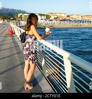 La ragazza parla con gli amici mentre guarda il bellissimo mare toscano. Foto Stock