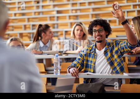 Studente di sesso maschile alzando la mano per una domanda al lezione in classe universitaria Foto Stock