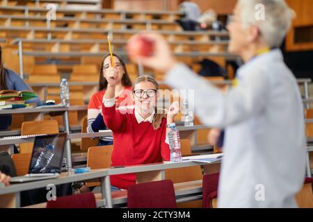 Studente di sesso maschile alzando la mano per una domanda al lezione in classe universitaria Foto Stock