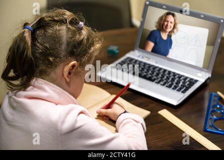 Capretto apprendimento virtuale con insegnante da laptop, bambina studia online in camera, tutor insegna bambino prescolare durante la quarantena. Concetto di distanza Foto Stock
