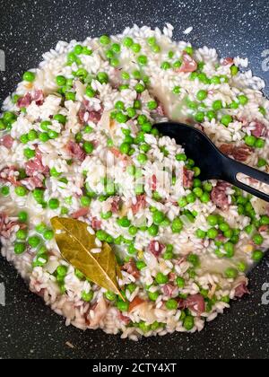 Primo piano - cottura in padella nera di risotti cremosi con piselli, cipolla e prosciutto Foto Stock