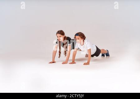 Foto a tutta lunghezza di ragazzo e ragazza adolescenti attivi che fanno push-up isolati su sfondo grigio, bambini impegnati nello sport. Foto Stock