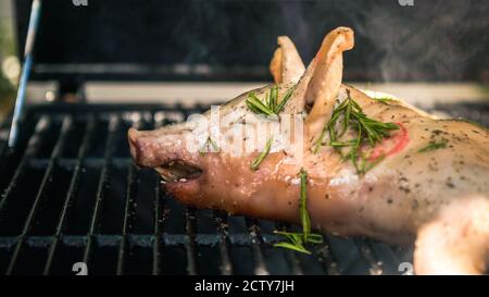 BBQ maiale intero alla griglia in casa giardino. Cucina casalinga di maiale arrosto croccante. Primo piano di arrosto di maialino su una spiedo, carne alla griglia spagnola. Foto Stock