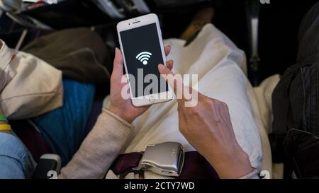 Donna asiatica che tiene lo smartphone e riceve il wi-fi gratuito disponibile all'interno di un aereo in viaggio. Il viaggiatore si siede all'interno dell'aereo utilizzando il telefono Foto Stock