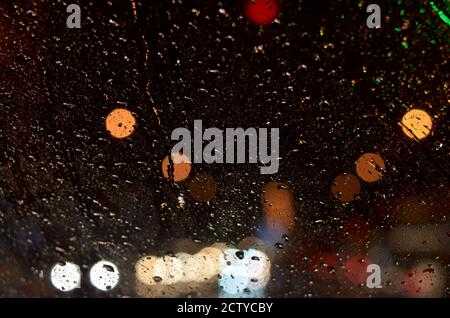 Gocce di pioggia sul vetro della macchina illuminata da lampioni di strada di notte. Foto Stock
