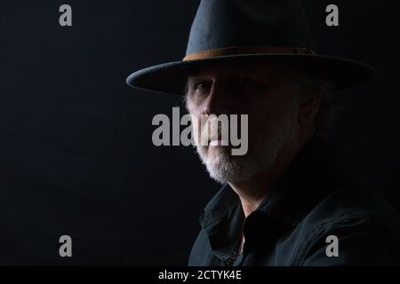 Ritratto in primo piano di un uomo di mezza età in un cappello occidentale largo-brimmed su uno sfondo scuro Foto Stock