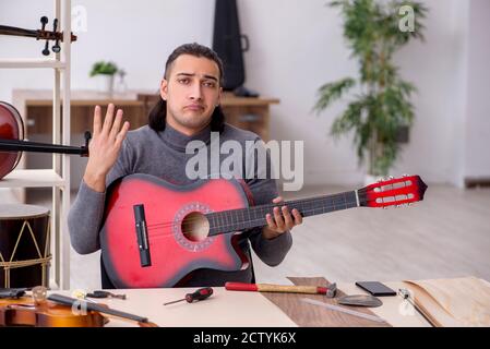 Giovane uomo riparatore che ripara la chitarra in officina Foto Stock