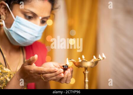 Fuoco selettivo sulle mani, donna indiana in maschera medica lanterna di illuminazione o lampada Diya durante il festival a casa - concetto di festival tradizionale Foto Stock