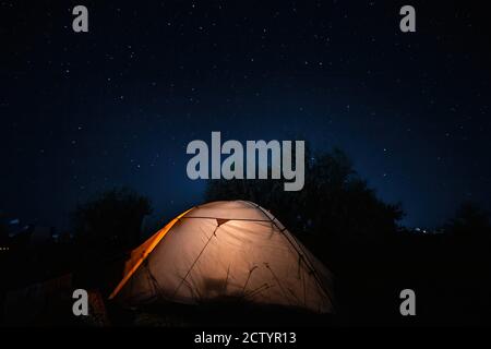 Tenda con luce sulla campagna di notte con stelle. Tenda gialla illuminata sull'erba sotto un bel cielo. Concetti di viaggio e avventura. Foto di alta qualità Foto Stock