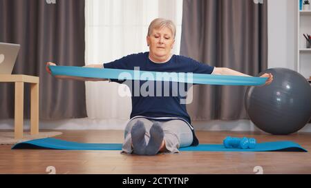 Allenamenti di donne anziane con banda di resistenza seduta sul tappetino yoga. Pensionata anziana donna stretching fitness vivere uno stile di vita sano in pensione, la formazione a casa esercizio Foto Stock