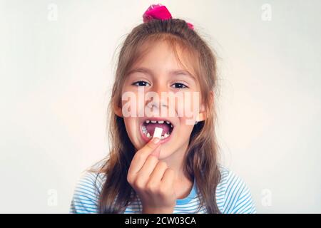 pulizia dei denti con gomma da masticare. la ragazza mette in bocca aperta i cuscinetti a forma di gomma bianca. cattiva abitudine, abitudine nociva, abitudine perniciosa, abitudine malsana Foto Stock