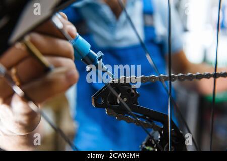 Assemblaggio di biciclette in officina, uomo che oliva la catena Foto Stock