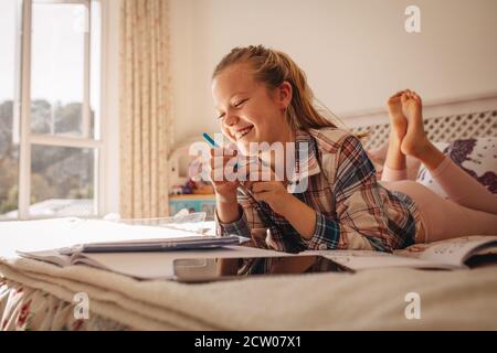 Ragazza sorridente sdraiata a letto con libri. Ragazza che studia mentre si sdraia a letto a casa. Foto Stock