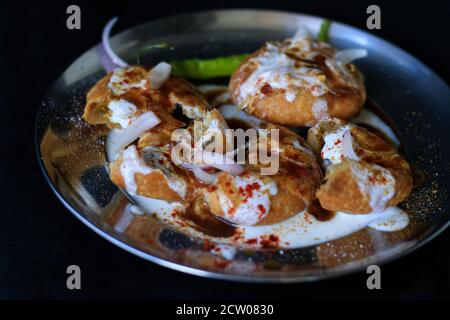 Indiano fritto chat kachori sormontato con cagliata e SEV e cipolle su uno sfondo nero con peperoncini verdi e rossi. Foto Stock