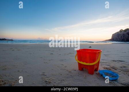 I giocattoli abbandonati sulla spiaggia lasciati su una spiaggia vuota salutano l'alba presto in una mattinata estiva a Little Beach, Scotts Head, New South Wales, Australia Foto Stock