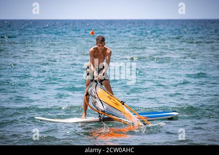 Giovane uomo che cerca di salire la sua vela windsurf Foto Stock