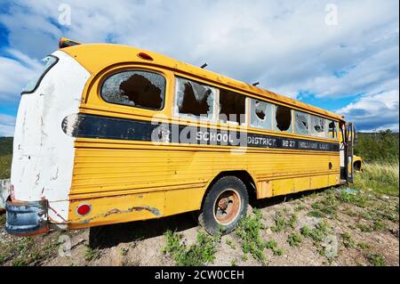 Vecchio autobus scolastico americano vandalizzato giallo con finestre di vetro rotte su un sito di scarico governativo vicino al lago Chilco, British Vancouver, Canada Foto Stock