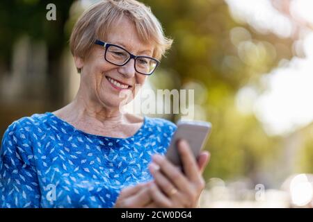 Donna anziana felice che usa il telefono cellulare all'aperto Foto Stock