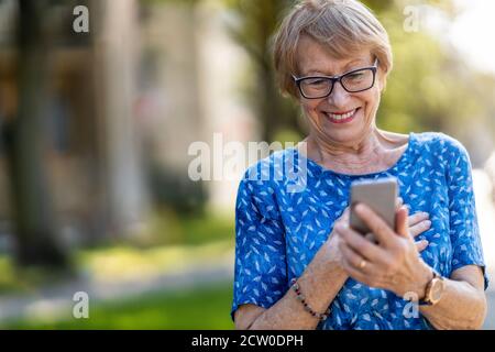 Donna anziana felice che usa il telefono cellulare all'aperto Foto Stock