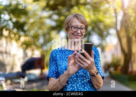 Donna anziana felice che usa il telefono cellulare all'aperto Foto Stock