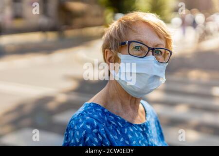 Ritratto di donna anziana che indossa una maschera protettiva per il viso all'aperto città Foto Stock