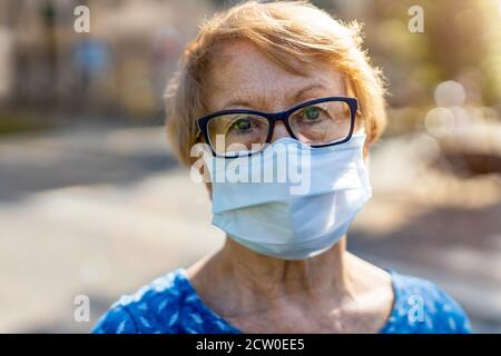 Ritratto di donna anziana che indossa una maschera protettiva per il viso all'aperto città Foto Stock