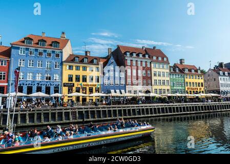Copenaghen, Danimarca - 27 agosto 2019: Persone che bevono su un bar con terrazza e una barca a vela con turisti lungo un canale a Nyhavn, Copenaghen, D. Foto Stock