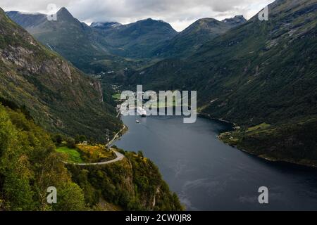 Geiranger fiordo con una grande nave da crociera nel porto e un piccolo traghetto per auto che arriva in una buia giornata estiva, la Norvegia Foto Stock