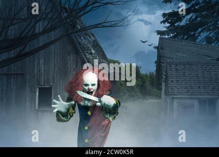 un clown pazzo con un coltello in mano davanti a una scena spaventosa Foto Stock