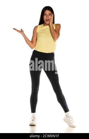 Giovane donna advertising stupito in leggings su sfondo bianco Foto Stock