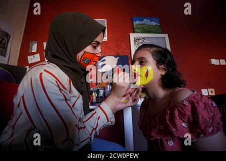 La ragazza palestinese Ranin al Zeriei (19), usa la vernice ad acqua mentre dipinge una maschera sul viso di una giovane ragazza. Nella striscia di Gaza meridionale della città di Deir al Balah, 25 settembre 2020. Per sensibilizzare l'opinione di indossare una maschera protettiva nello scoppio del Coronavirus (Covid-19) a Gaza. (Foto di Yousef Masoud/INA Photo Agency) Foto Stock