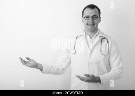 Studio girato di giovane felice medico di uomo muscolare sorridente mentre indossare occhiali e mostrare qualcosa Foto Stock