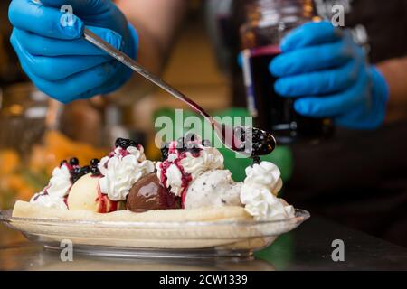 Preparazione di crosta artigianale di Banana italiana con gelato, panna montata, ciliegie e cuocie di lingua di gatto. Foto Stock