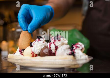 Preparazione di crosta artigianale di Banana italiana con gelato, panna montata, ciliegie e cuocie di lingua di gatto. Foto Stock