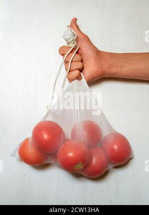 Mano maschile che tiene i pomodori in un ecobag riutilizzabile di fronte bianco sfondo Foto Stock