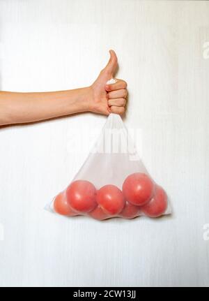 Mano maschile che tiene i pomodori in un ecobag riutilizzabile di fronte bianco sfondo Foto Stock