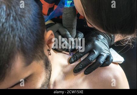 Primo piano di un'artista di tatuaggio femminile che tatuava di un uomo spalla Foto Stock