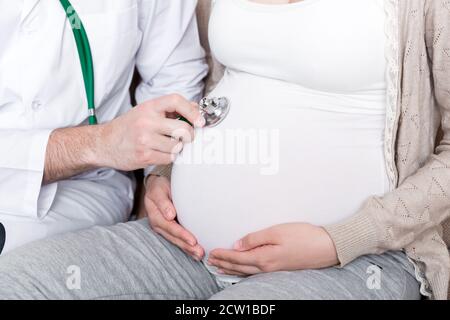 Il medico sta controllando il ventre della donna incinta con uno stetoscopio. Il medico sta ascoltando un battito cardiaco di un bambino. Foto Stock
