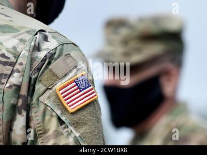 Bandiera americana sul braccio del soldato e sui soldati statunitensi che indossano maschere facciali di protezione. Quarantena in esercito. Forze militari degli Stati Uniti d'America. Foto Stock