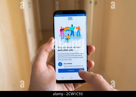 Un uomo che tiene in mano uno smartphone che mostra l'app NHS Test and Trace per Covid-19 con un dito che punta e utilizza l'applicazione, Regno Unito Foto Stock