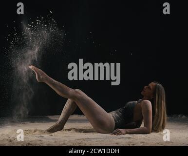 Ballerina con lunghi capelli biondi che gettano polvere, farina, polvere su fondo nero. Foto Stock