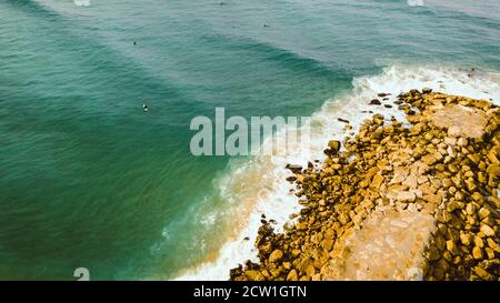 Molo roccioso. Oceano verde con surfisti. Vista aerea. Costa da Caparica Portogallo Foto Stock
