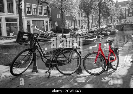 Una foto di una bici rossa sul ponte sul canale di Amsterdam. Lo sfondo è bianco e nero. Foto Stock