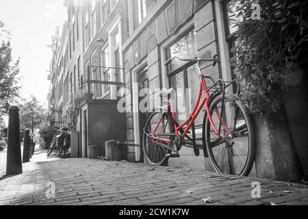 Una foto di una sola bici rossa sulla strada vicino al canale di Amsterdam. Lo sfondo è bianco e nero. Foto Stock