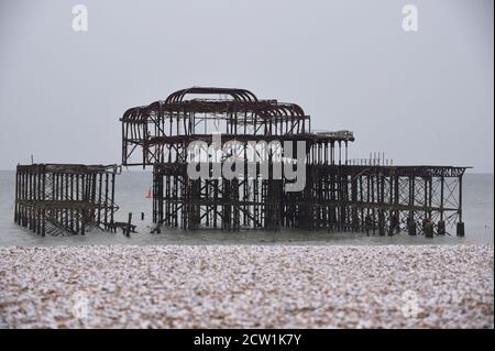 Una mattina fredda sulla spiaggia di Brighton, con neve sui ciottoli e le rovine del vecchio molo sullo sfondo. Foto Stock